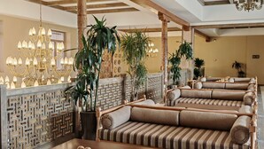 A hotel lobby with wooden benches, a patterned wall, and a chandelier.