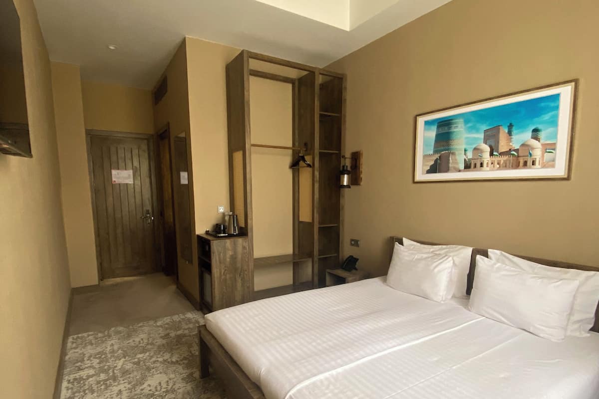 A hotel room with a large bed, a mirror, a painting, and a wardrobe.