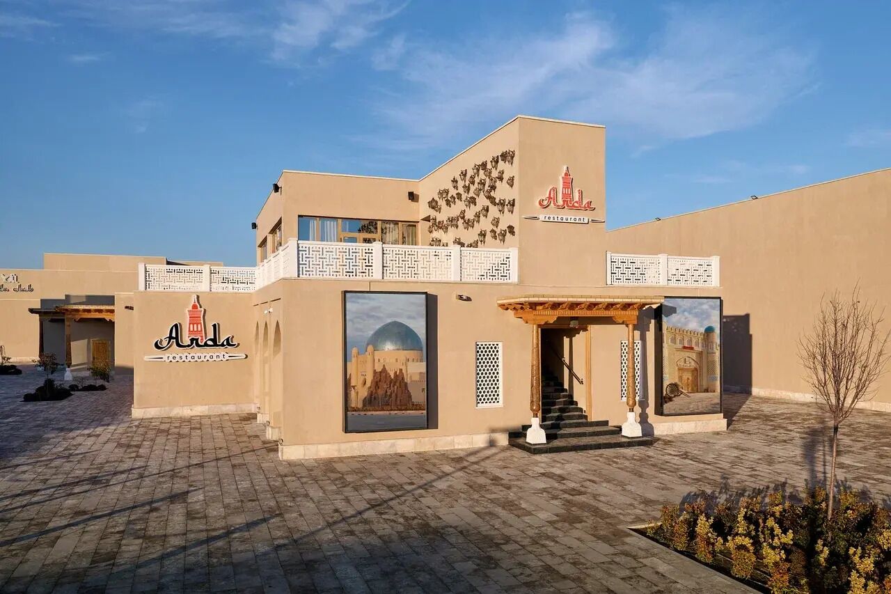 Een gebouw met een bord waarop 'Al Arda restaurant' staat, en een groot raam dat een woestijnlandschap toont.