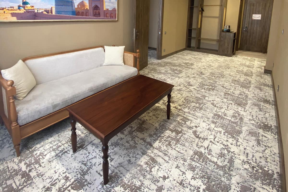 Une chambre d’hôtel avec un canapé, une table basse, une moquette à motifs, un tableau représentant un paysage urbain et une porte en bois.