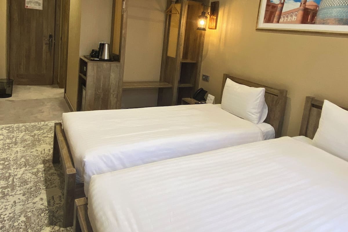 A hotel room with two beds, a wooden wardrobe, a desk with a chair, a coffee maker, and a framed picture on the wall.