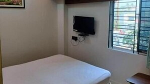 A single bed with a wooden frame, a mounted television, and a window with metal bars. - Hotel Epar Bangla (Agartala)