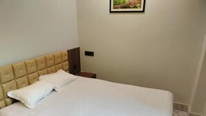 A neatly made bed with a headboard, a bedside table, and a framed picture on the wall. - Hotel Epar Bangla (Agartala)