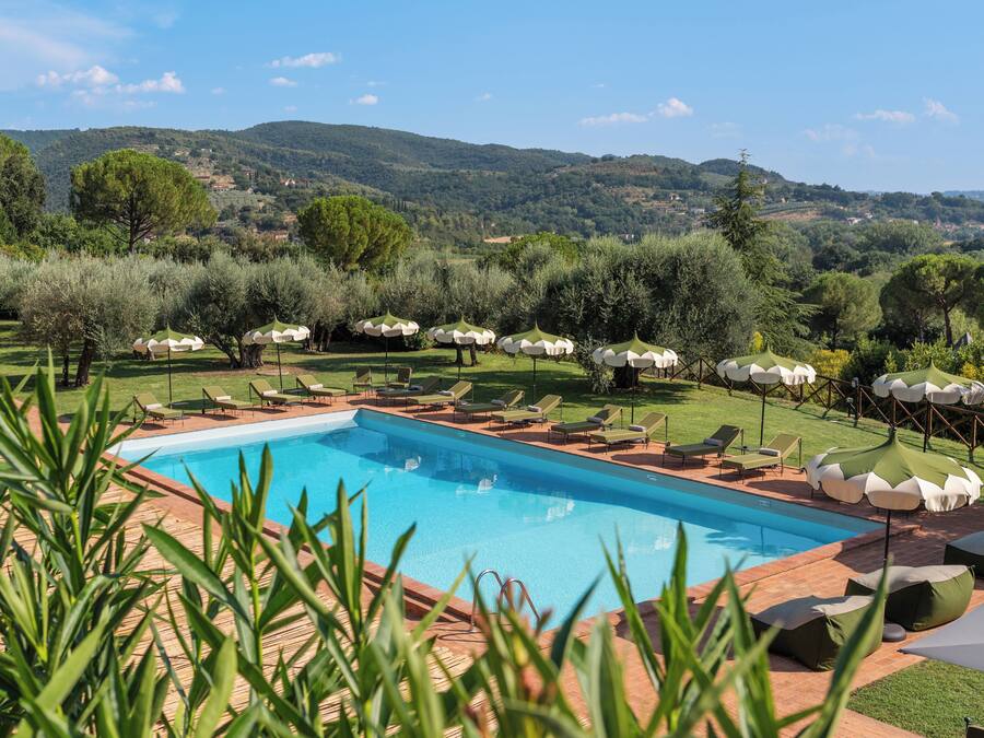 Ein Swimmingpool mit Liegestühlen und Sonnenschirmen, umgeben von Grünflächen und Hügeln.