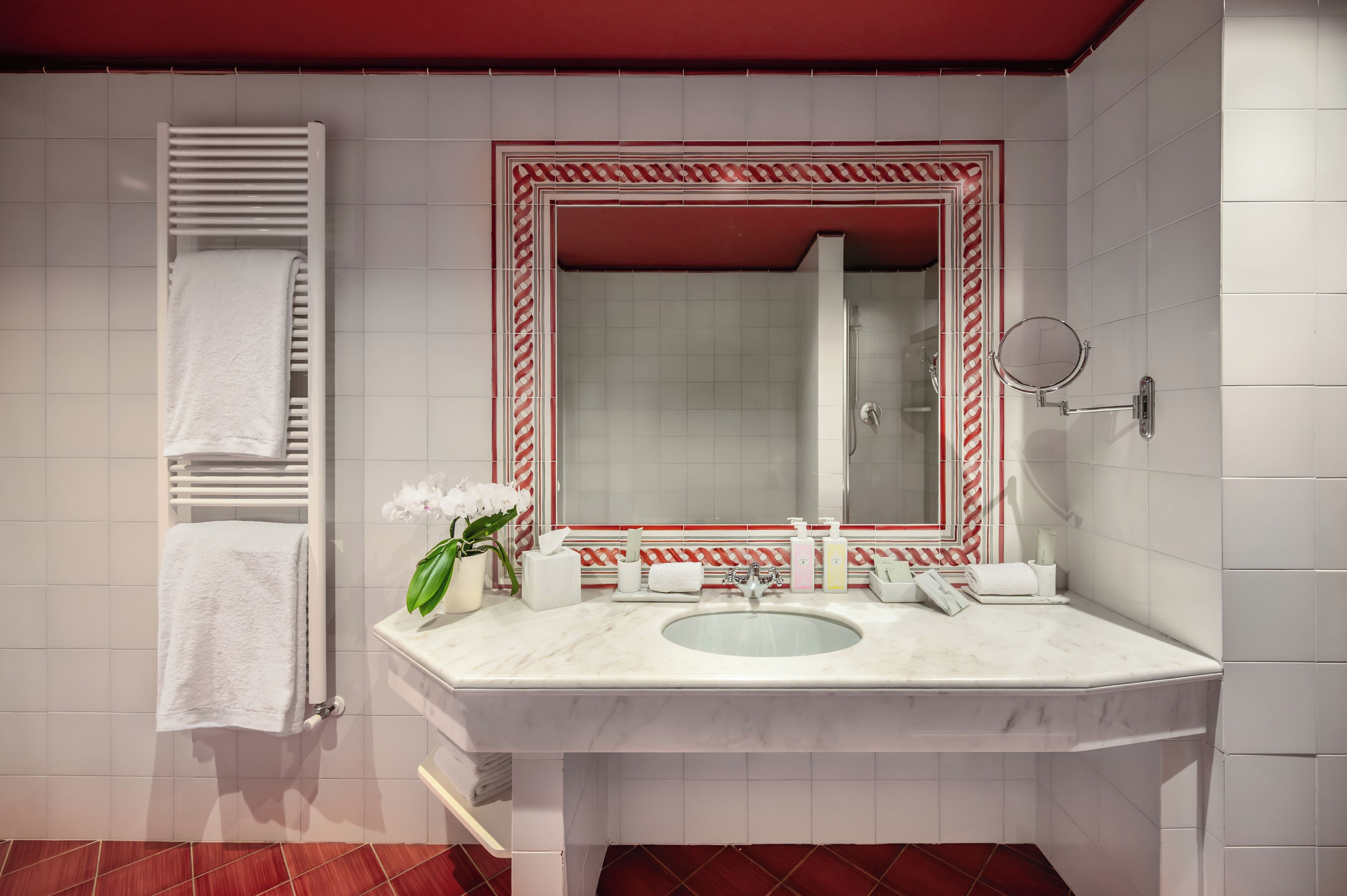 Un baño moderno con un lavabo blanco, espejo, toallero y espejo con marco rojo.