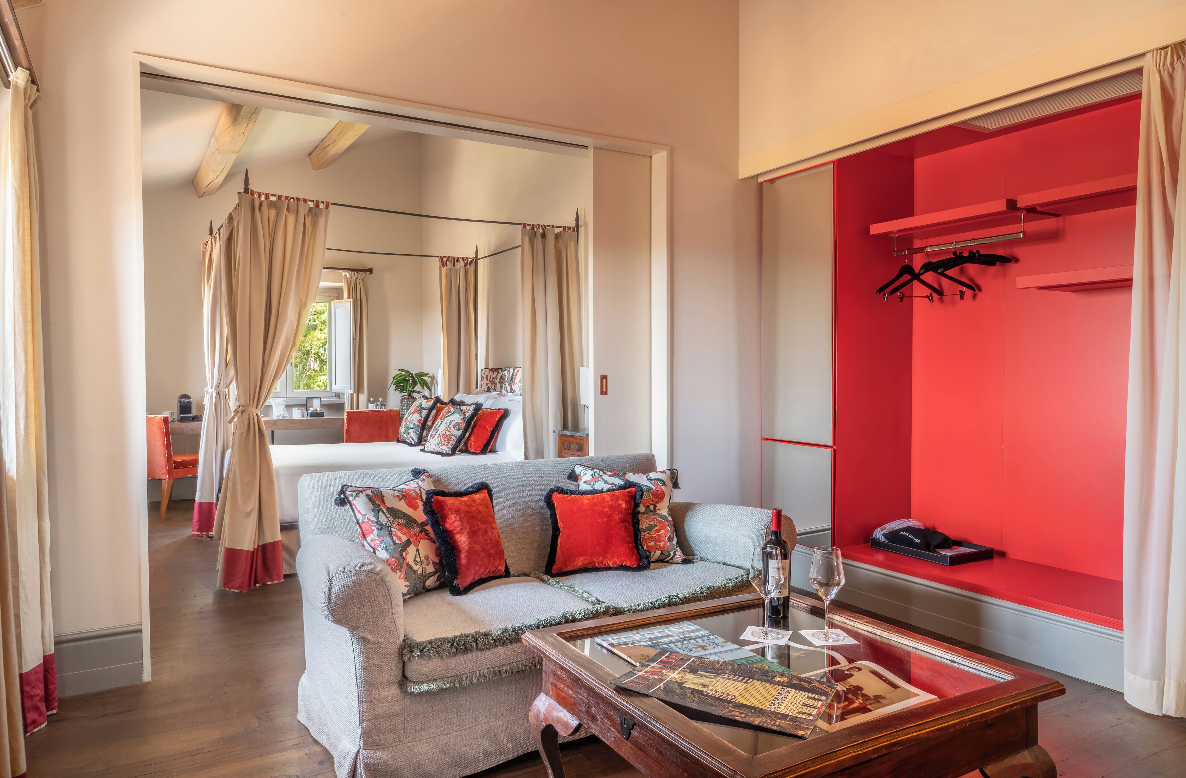 Un dormitorio con cama, sofá, mesa de centro con revistas y una pared de acento roja.