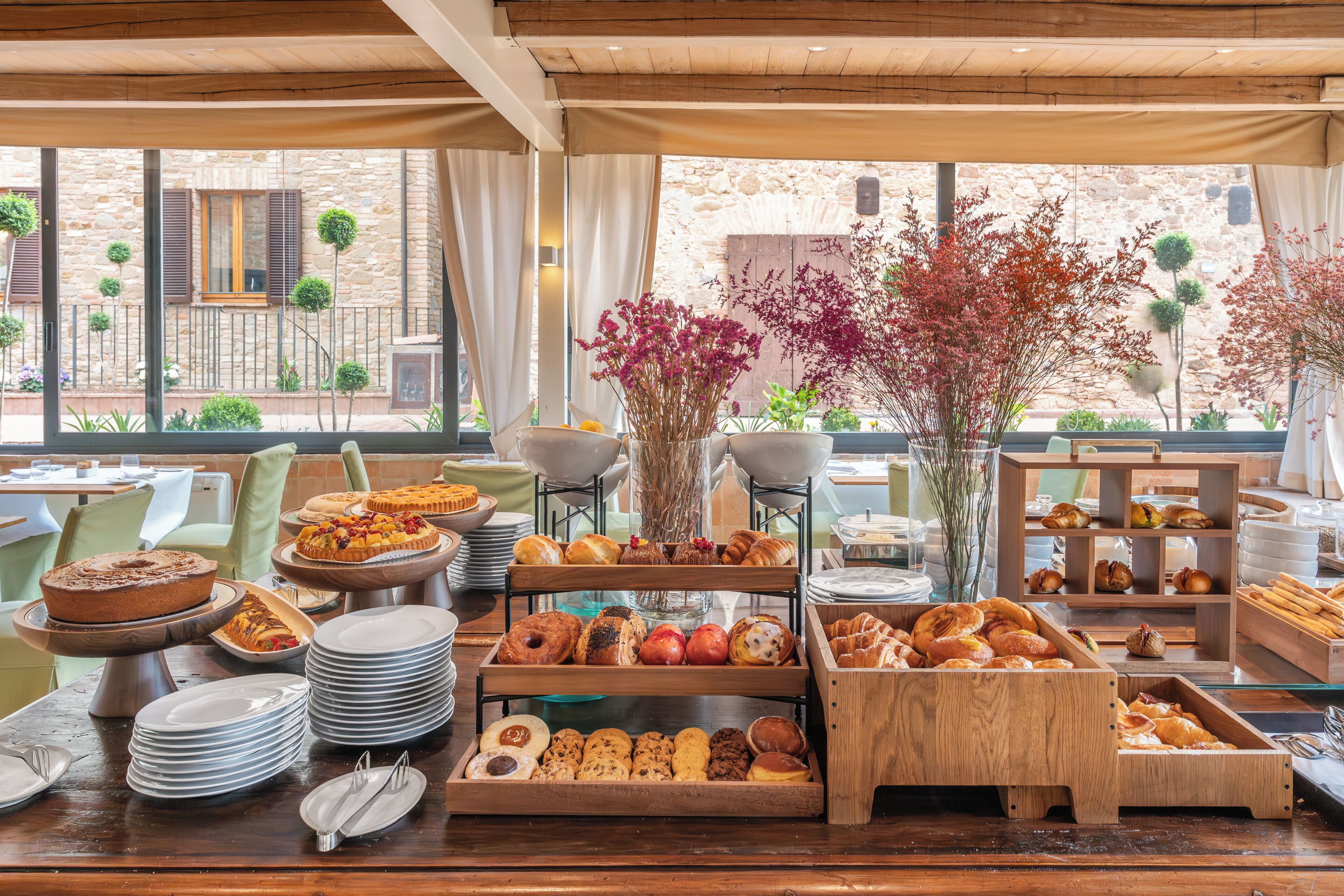 A breakfast buffet with various pastries and fruits, a wooden table, and a view of the outside.