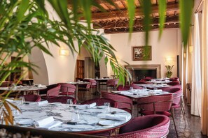 A restaurant with round tables, red upholstered chairs, and a fireplace.