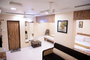 A hotel room with a bed, a sofa, a ceiling fan, a mirror, and a wooden panel wall. - Park View Residency (Bhuj)