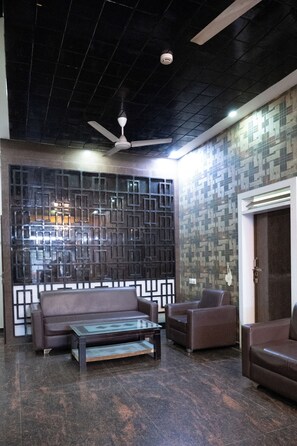 A modern lobby with a ceiling fan, a patterned wall, a brown leather sofa, a glass coffee table, and a door. - Park View Residency (Bhuj)