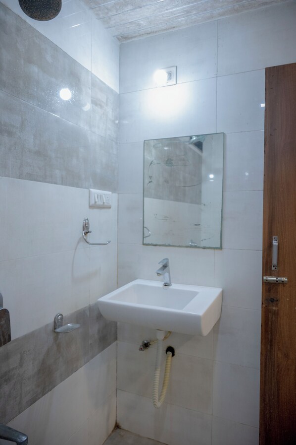 Un baño con lavamanos blanco, un espejo, un cabezal de ducha y una puerta de madera.