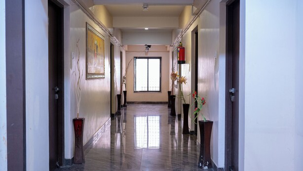 A hallway with a polished floor, framed artwork on the walls, and potted plants. - Park View Residency (Bhuj)