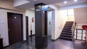 A hotel lobby with a marble floor, a staircase with a red railing, and a 'No Smoking' sign on a pillar. - Park View Residency (Bhuj)