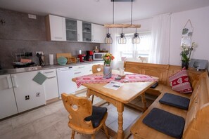 A modern kitchen with white cabinets, a wooden dining table, and a bench with cushions. - A charming guesthouse with 5 vacation apartments in a quiet location on the outskirts of town. (Scheidegg)