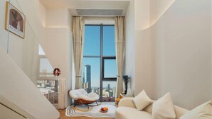 Una sala de estar moderna con sofá, sillón, vistas a la ciudad a través de amplias ventanas y un patrón de suelo tipo espiga.