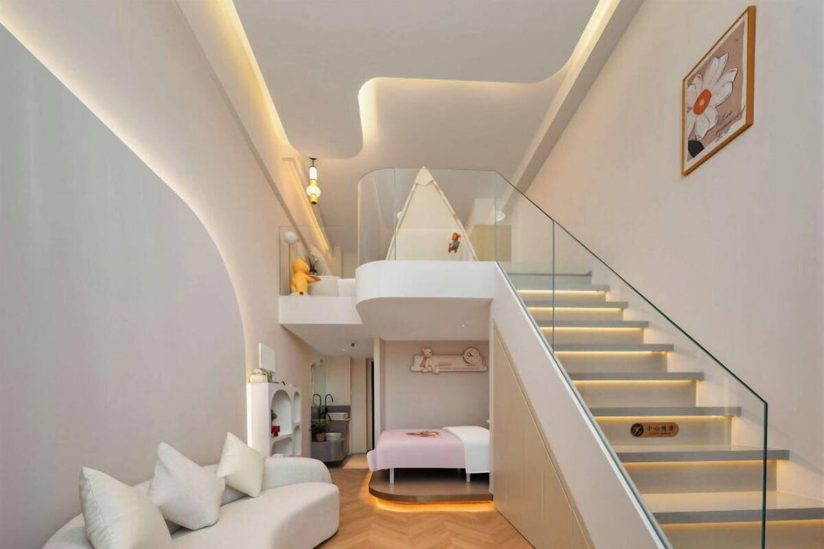 Um interior moderno com um sofá curvo, uma cama, uma escada e uma pequena cozinha.