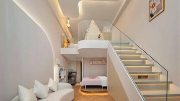 Un interior moderno con un sofá curvo, una cama, una escalera y una pequeña cocina.