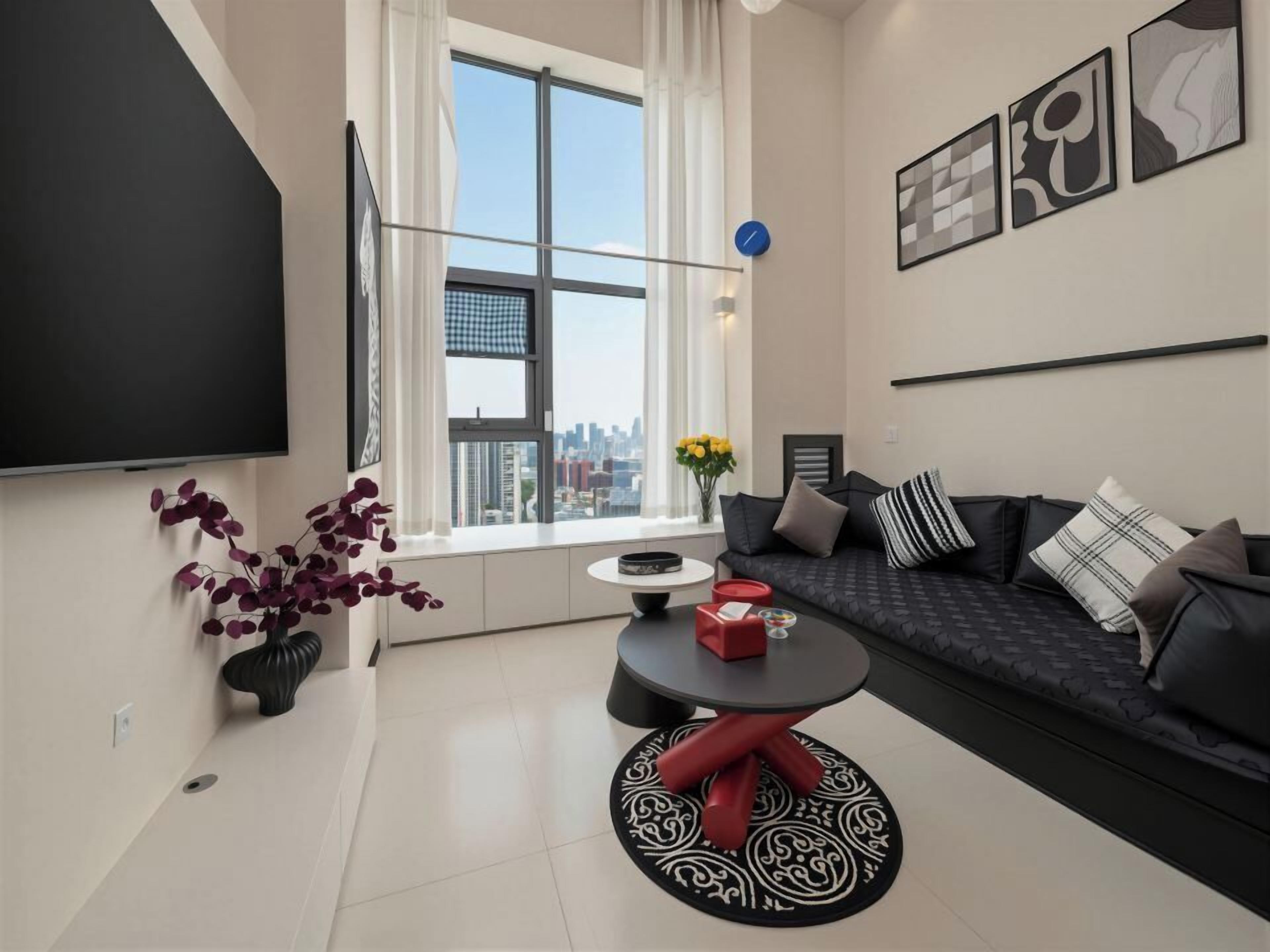 A modern living room with a sofa, a coffee table, a TV, and a window with a city view.