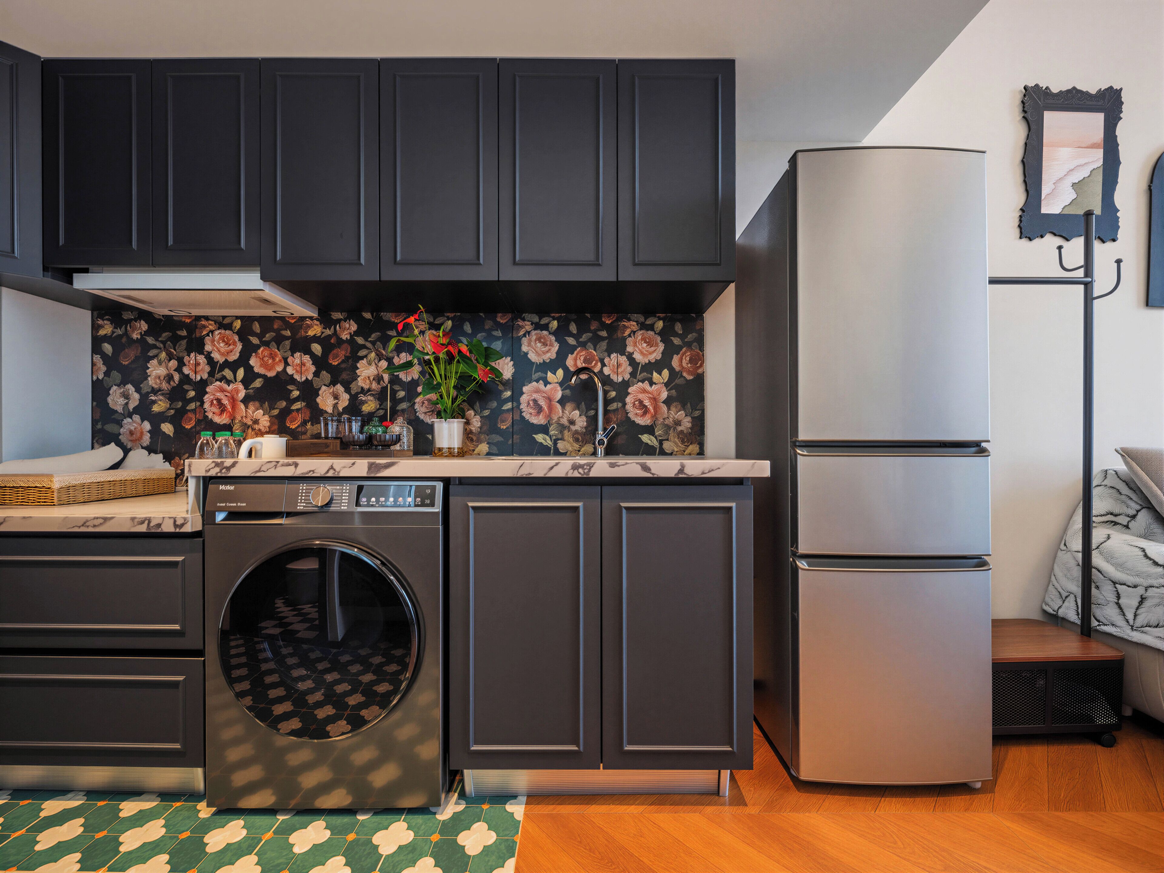 A compact kitchen with dark cabinets, a built-in washing machine, a refrigerator, and a floral backsplash.