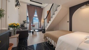 Una habitación de hotel moderna con una cama, un escritorio, una silla, un sofá, una escalera y vistas de la ciudad.