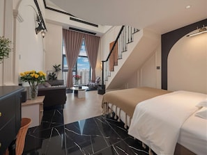 Quarto de hotel moderno com uma cama, uma escrivaninha, uma cadeira, um sofá, uma escada e vista para a cidade.
