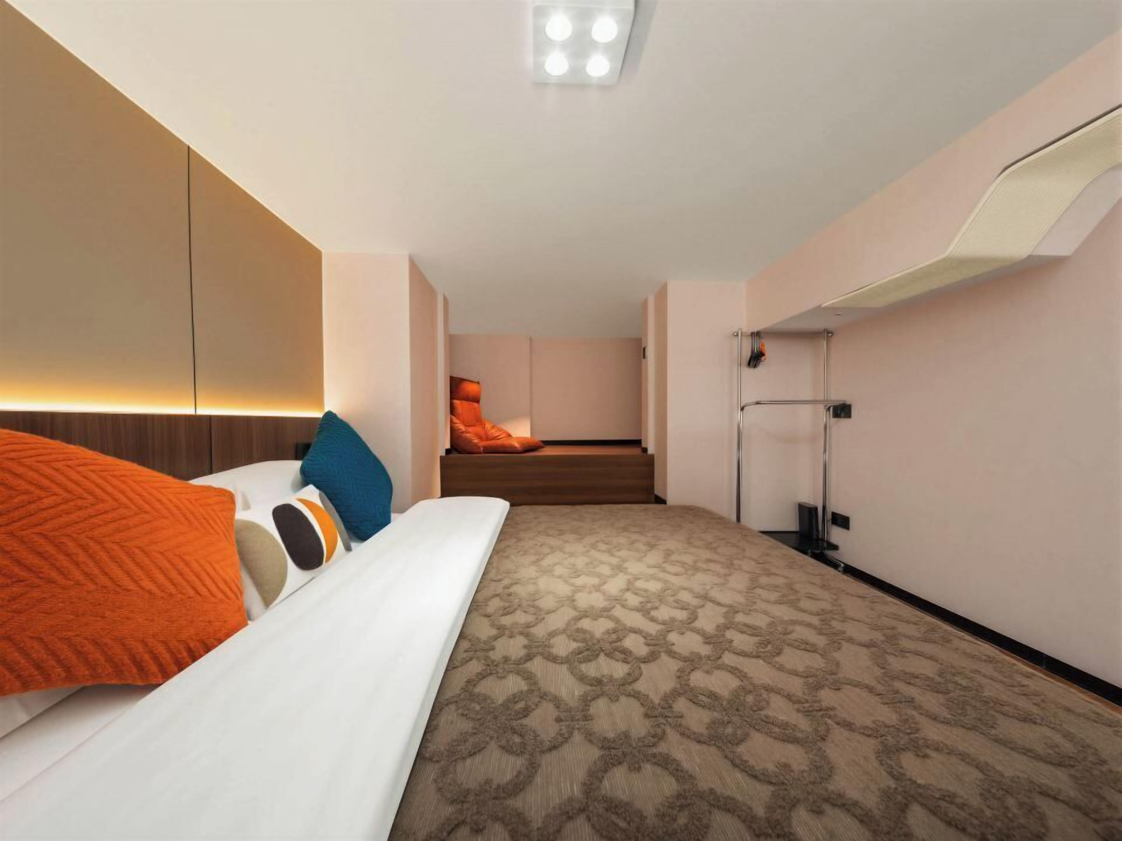 Una habitación de hotel con cama, escritorio, silla, lámpara y ventana.