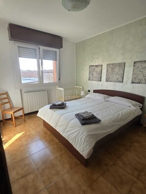 Ein Schlafzimmer mit einem Bett, einem Sessel, einem Babybett und drei Bildern an der Wand.