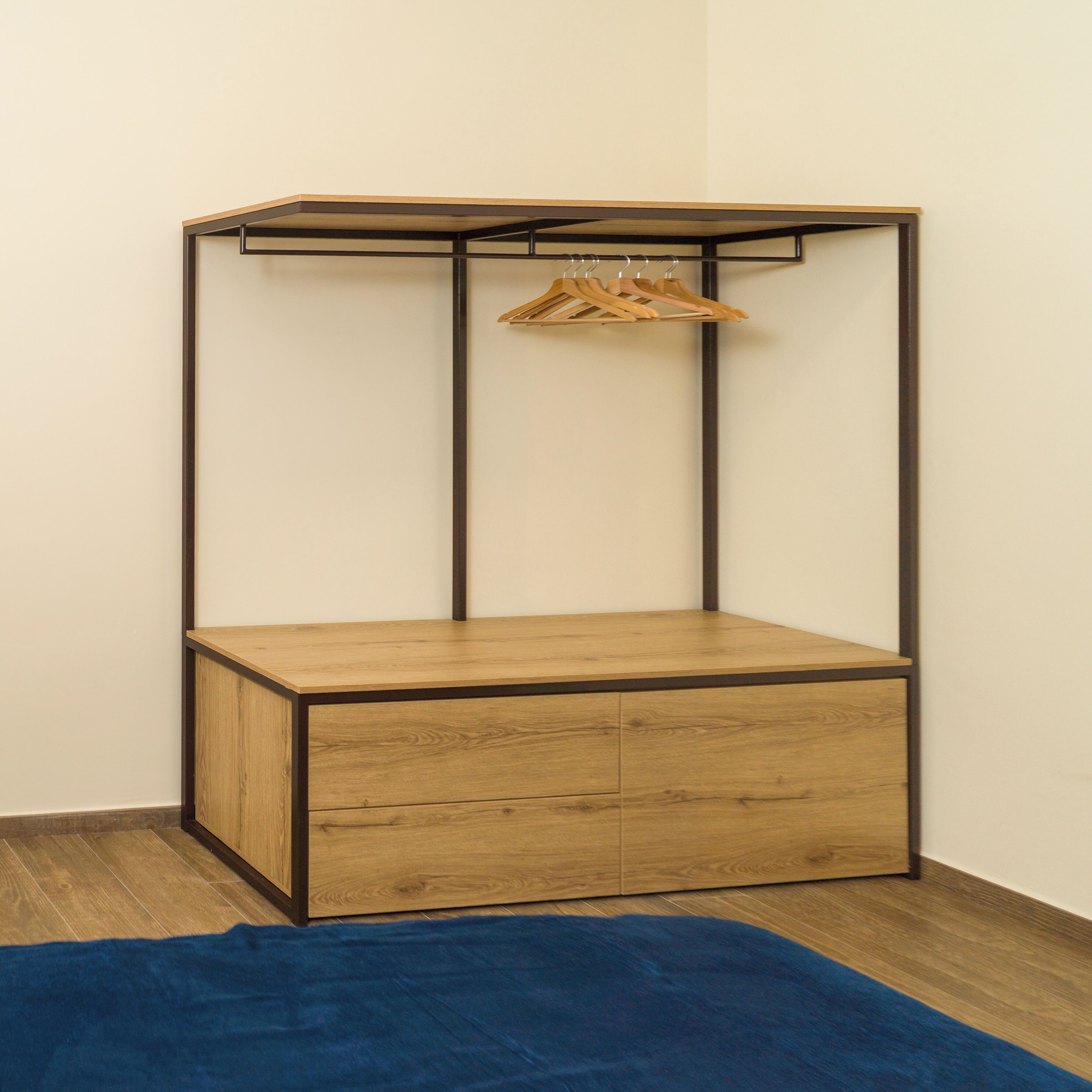 A corner room with a wooden cabinet, a hanging clothes rack, and a blue rug.