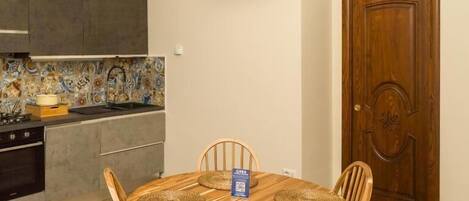 A compact kitchen with a tiled backsplash, a flat-screen TV mounted above the counter, and a wooden dining table with woven placemats.