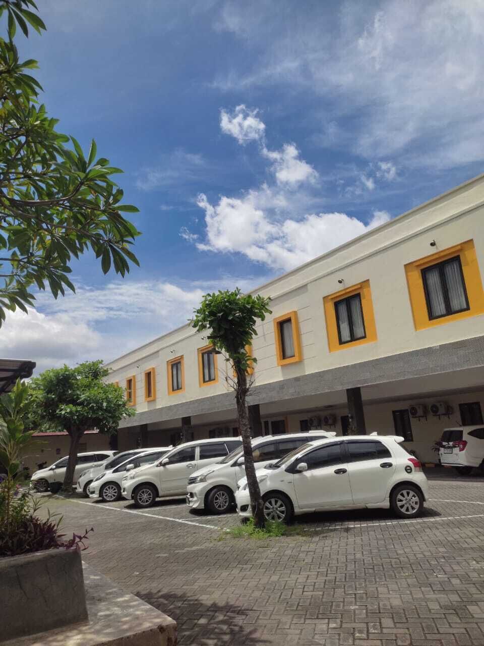 A parking lot with several white cars, a building with yellow trim, and a clear blue sky.