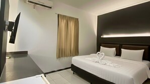 A hotel room with a bed, a flat-screen TV, an air conditioning unit, and a window with curtains.