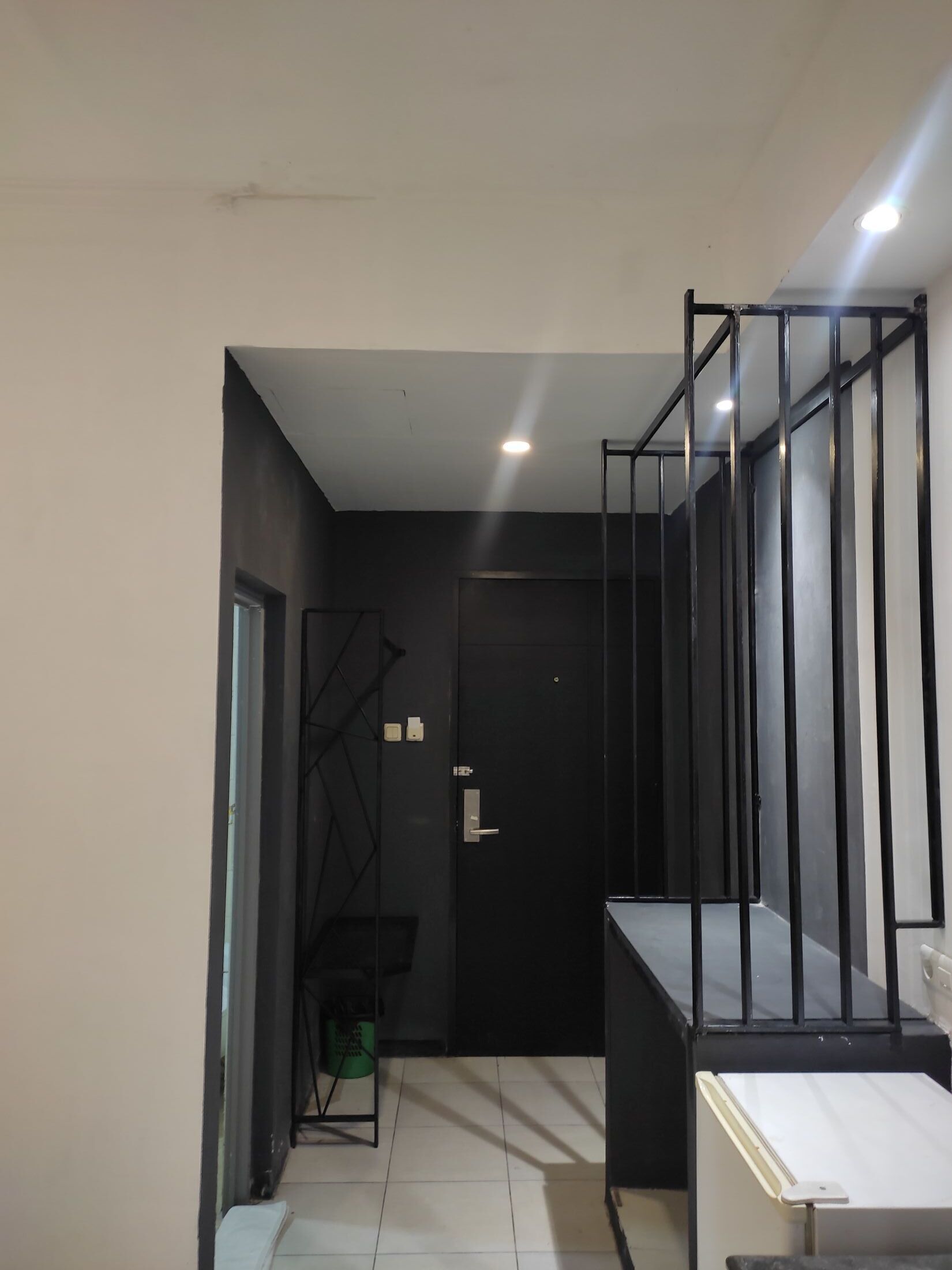 Un pasillo con una puerta negra, una escalera y una barandilla de metal.