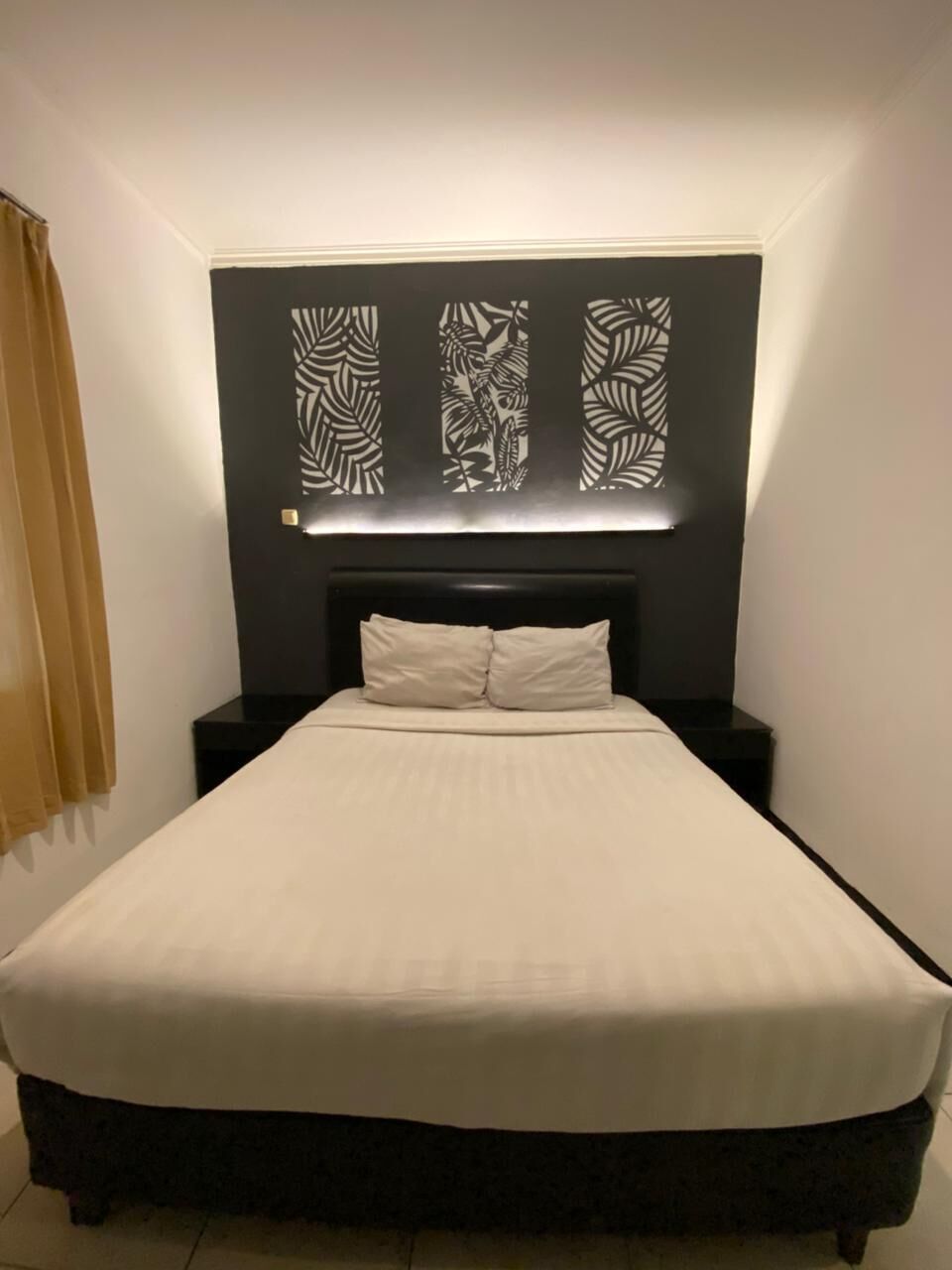A neatly made bed with a headboard, a bedside table, and a wall-mounted light fixture.