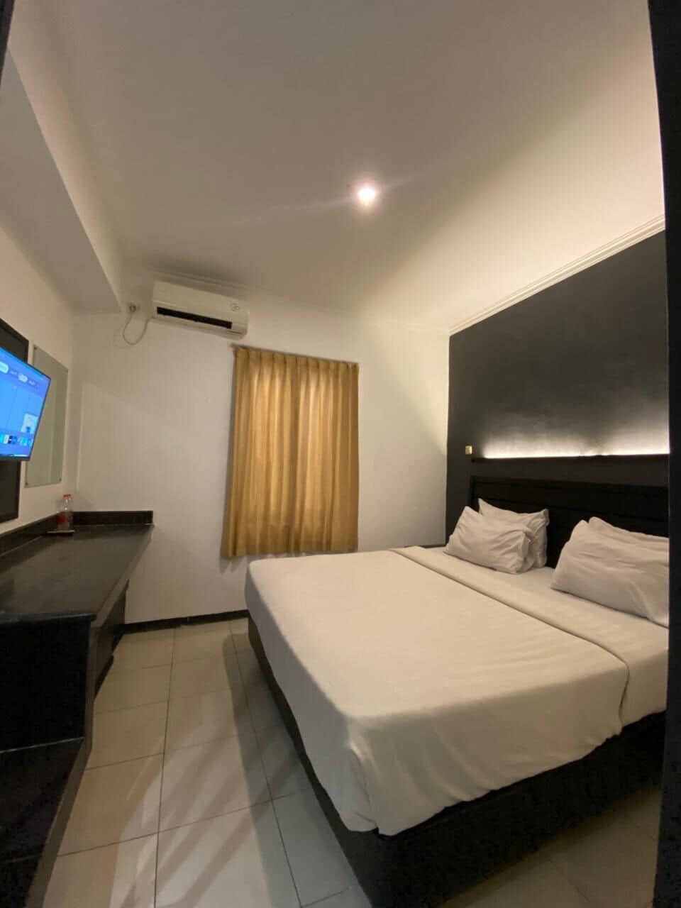 Ein Hotelzimmer mit Bett, Schreibtisch, Flachbildfernseher und einem Fenster mit Vorhängen.