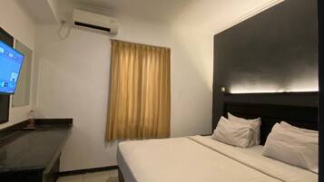 Ein Hotelzimmer mit Bett, Schreibtisch, Flachbildfernseher und einem Fenster mit Vorhängen.