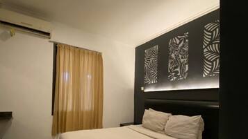 Quarto de hotel com cama, cortinas, cabeceira com painéis decorativos e luminária no teto.