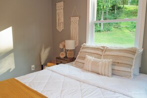 Une chambre à coucher avec un lit, une table de chevet, une lampe et des décorations murales en macramé.
