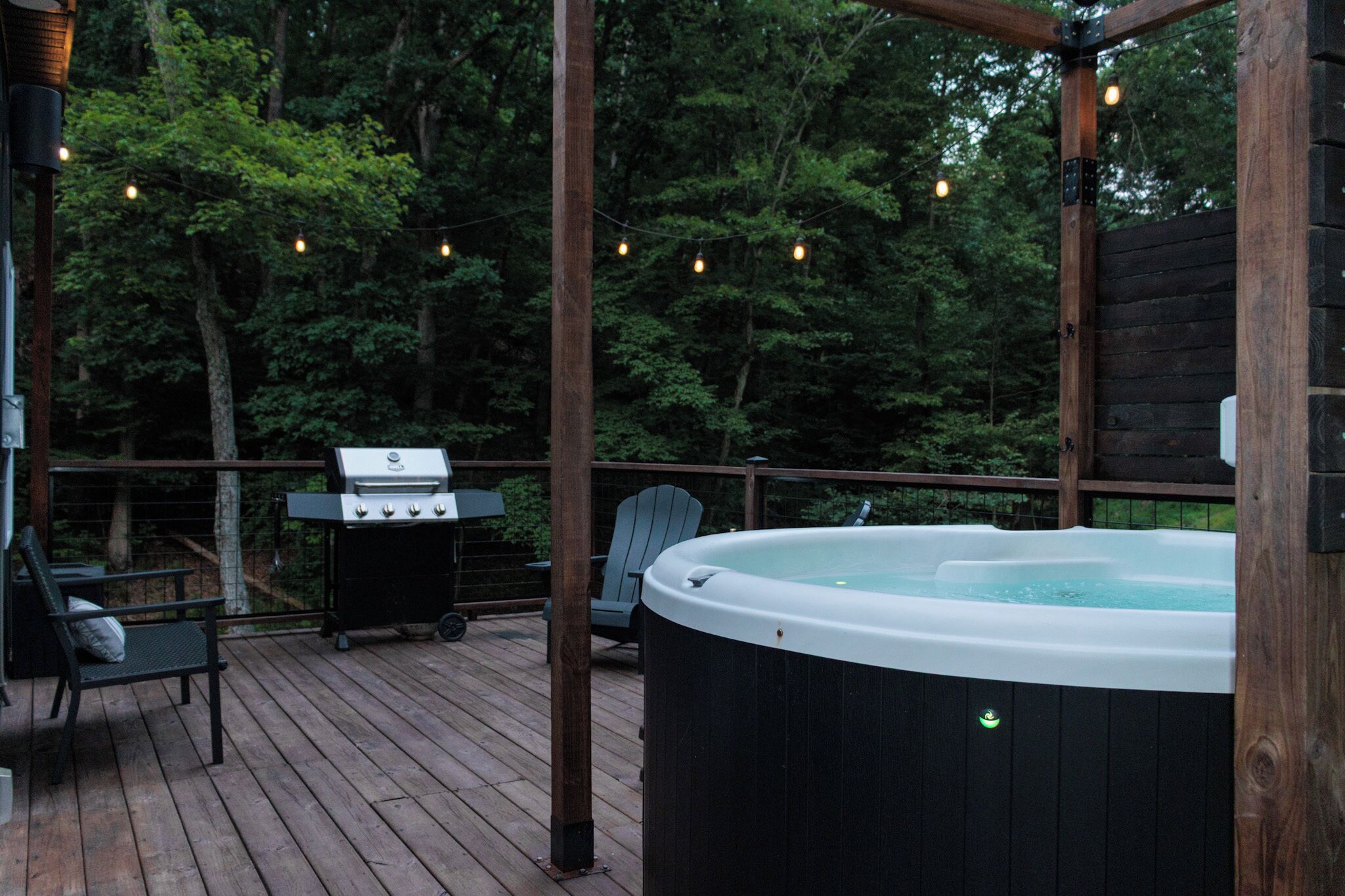 Eine Terrasse im Freien mit Whirlpool, Grill und Stühlen.