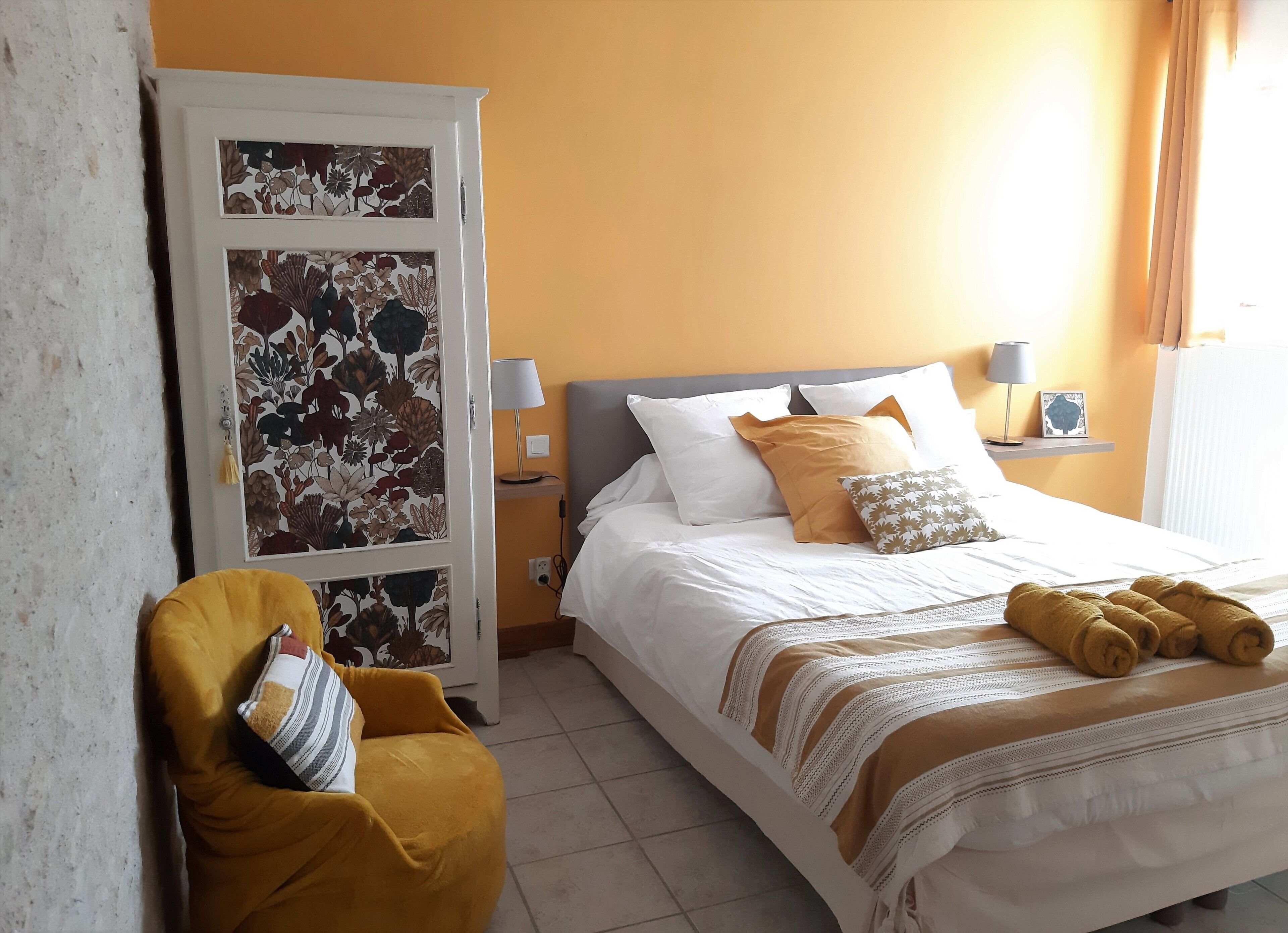 Hotelkamer met een bed, een stoel, een nachtkastje met lamp en een bloemen behang.