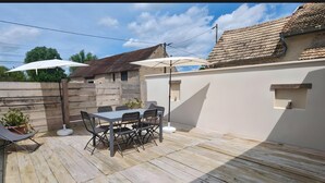 Une terrasse avec une table et des chaises, entourée d’une clôture en bois et d’un mur blanc.