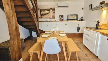 A dining area with a wooden table set for six, a white chair in the center, and a kitchen with a microwave and sink.