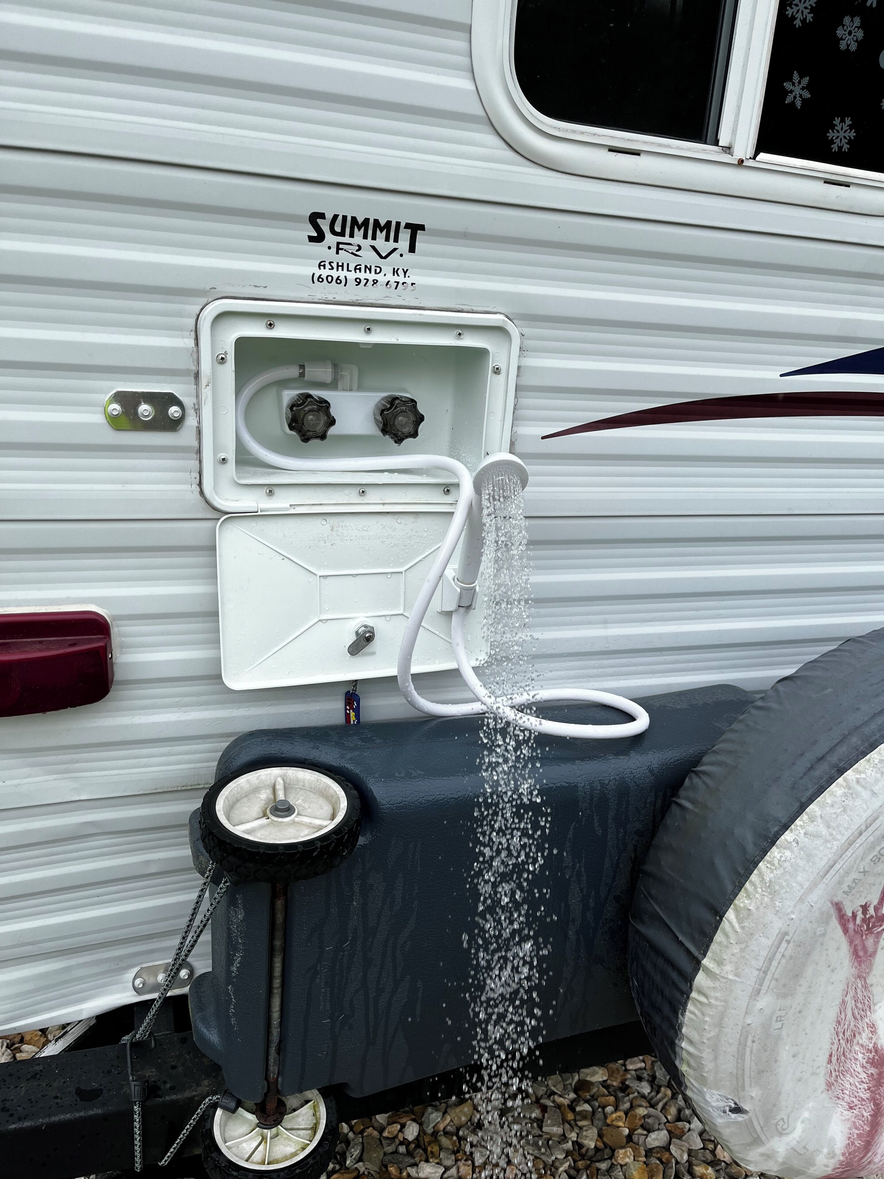 Ein Wasserhahn an einem weißen Wohnmobil der Marke SUMMIT RV, mit einer Telefonnummer.