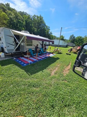 A recreational vehicle with a covered patio area, a picnic table, and a small ATV.