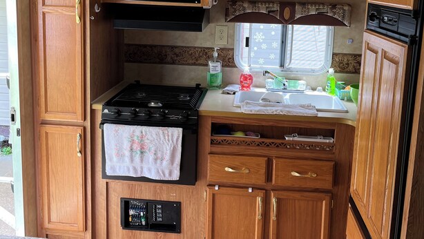 Cocina compacta para autocaravana con armarios de madera, microondas, estufa y pileta.