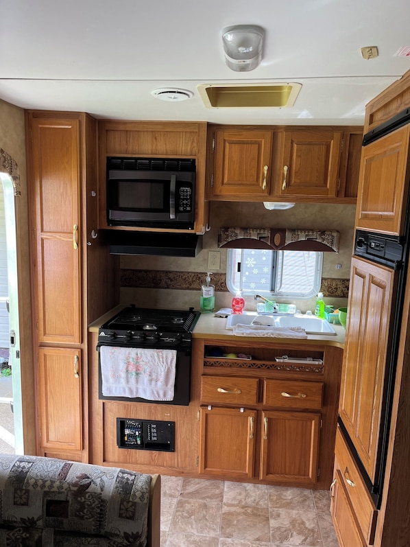 A compact RV kitchen with wooden cabinets, a microwave, a stove, and a sink.