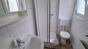 Een badkamer met een douche, toilet, wastafel en een raam.
