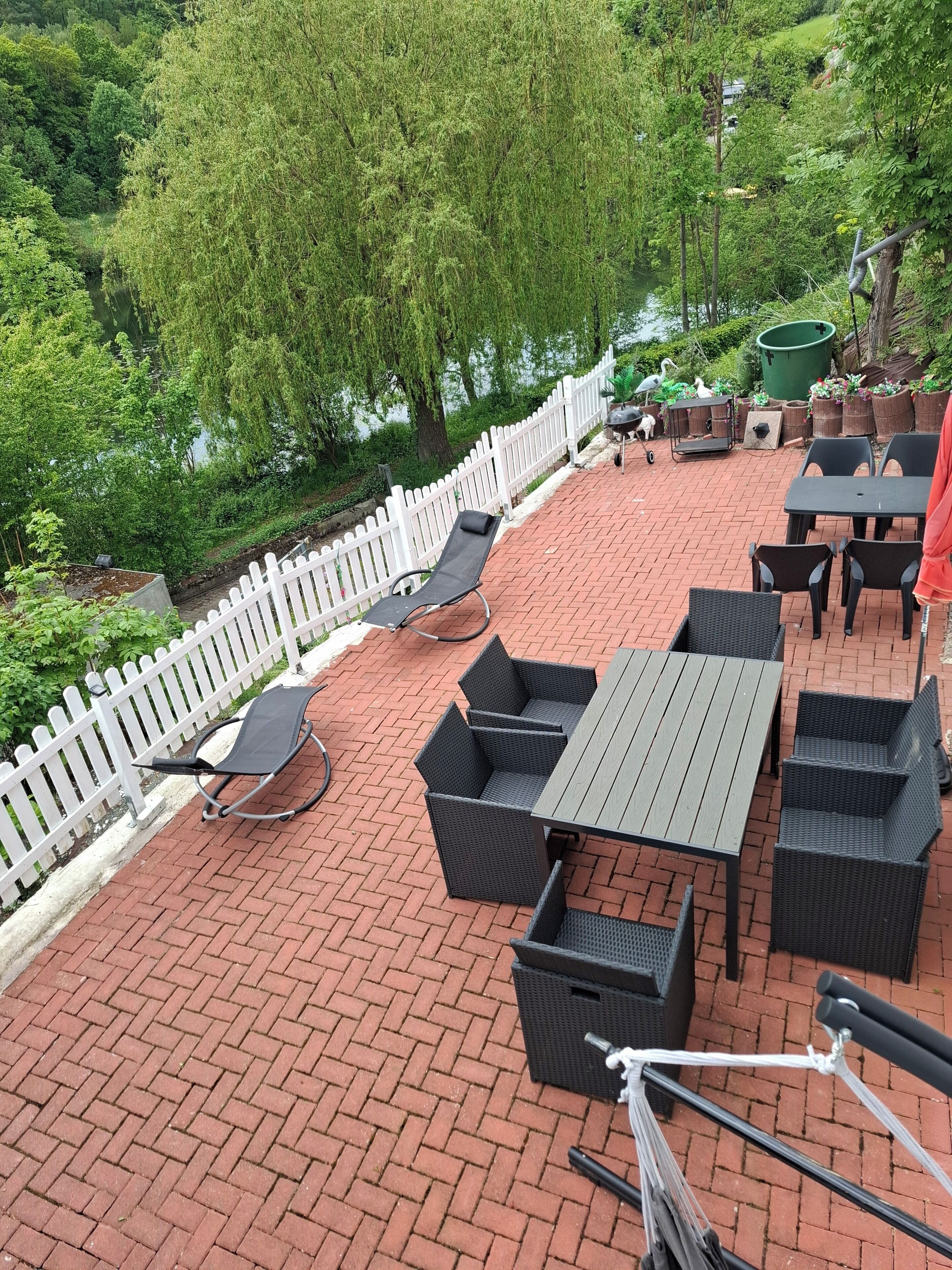 An outdoor patio with wicker furniture, a white picket fence, and a view of a river.
