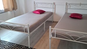 Een kamer met twee eenpersoonsbedden, een kamerbreed tapijt met dessin en een raam met gordijnen.