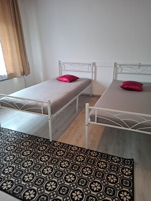 Ein Zimmer mit zwei Einzelbetten, einem gemusterten Teppich und einem Fenster mit Vorhängen.