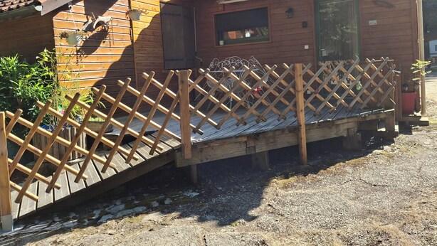 Una cabaña de madera con techo inclinado, una terraza de madera y una cerca de celosía.